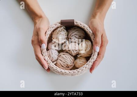 Female hands holding a crocheted basket with skeins of cotton yarn in natural tones and colors. Stock Photo