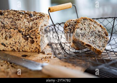 Freshly sliced multigrain bread in basket on wooden cutting board with kitchen kniffe. Close-up in front of bright window. Stock Photo