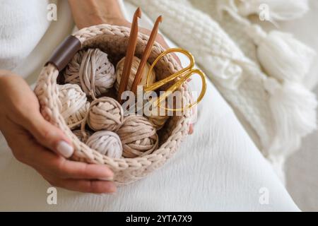 Female hands holding a crocheted basket with skeins of cotton yarn in natural tones  Stock Photo