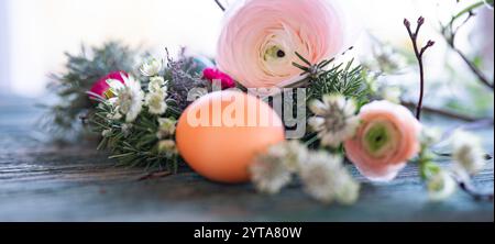 Easter egg in front of a herb nest with spring flowers on weathered rustic wooden table. Close-up with short depth of field. Horizontal easter background. Stock Photo