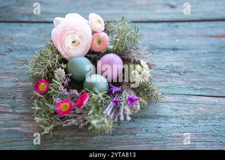 Colorful easter eggs in a herb nest with spring flowers on weathered rustic wooden table. Top view with space for text. Stock Photo