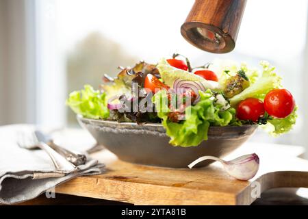 Fresh green salad in a ceramic bowl with tomato, onions and olives on wooden cutting board. Healthy nutrition concept for fitness and spring diet. Close-up. Stock Photo