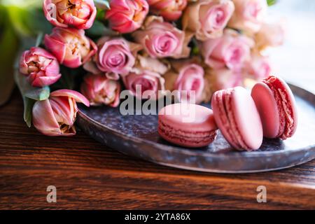 Beautiful pink roses and tulips with sweet delicacies. Sweet macaron pastries on a wooden table. Still life background for mother 's day and weddings. Close-up. Stock Photo