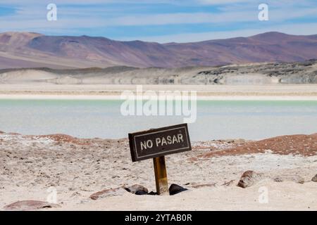 Sign reading 'No Pasar' at Piedras Rojas, a stunning landscape in the Atacama Desert, Chile. Featuring a vibrant mineral-rich lake and red-hued rocks Stock Photo