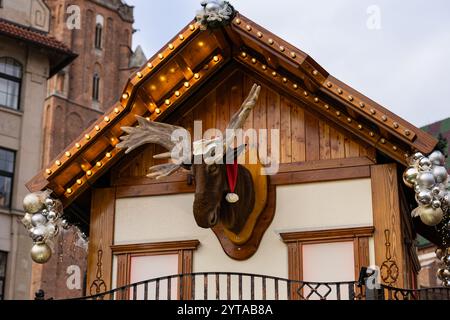 Cozy wooden house with a mounted talking moose head in a Santa hat telling Christmas stories, illuminated with festive lights at the Christmas Market Stock Photo
