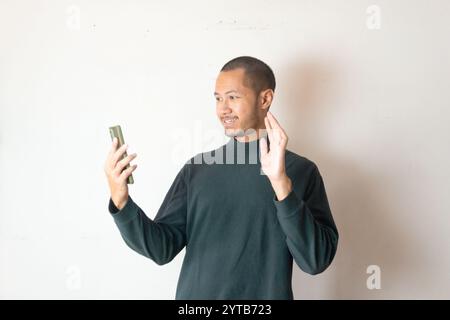 Young men wearing green sweater waving hand to smartphone calling friend on isolated white background Stock Photo