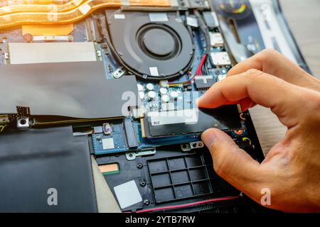 Laptop repair engineer PC computer and motherboard install random access memory ram ssd in computer lab top. The master installs the disk in his hands Stock Photo