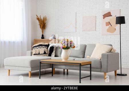 Cozy sofa and vase with wild flowers on coffee table in interior of ...