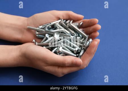 Female hands holding pile of different tap bolts and screws on blue background Stock Photo