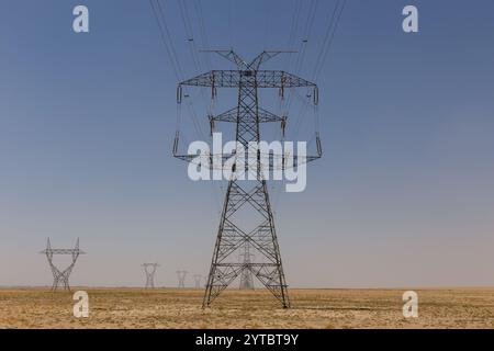 Tall transmission towers stretch across the barren landscape of Afghanistan, supporting electric power lines in a remote area. Stock Photo