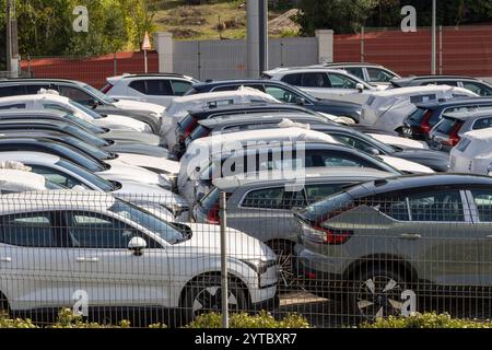 Rows of shiny new cars sit parked in a dealership storage area, some covered with protective sheeting, awaiting delivery to their new owners Stock Photo