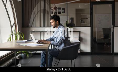 Serious Indian businessman sitting at desk, working on laptop Stock Photo