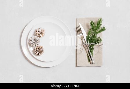 White plate with silver cutlery and Christmas decor on a white background. Festive serving. View from above. Preparing for Christmas dinner. Stock Photo