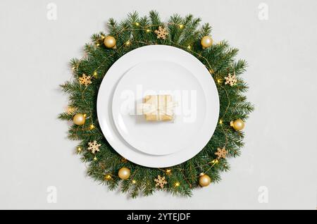 A small golden gift box in a white plate with Christmas wreath on a white background. New Year's table setting. Preparing for Christmas dinner. Top vi Stock Photo