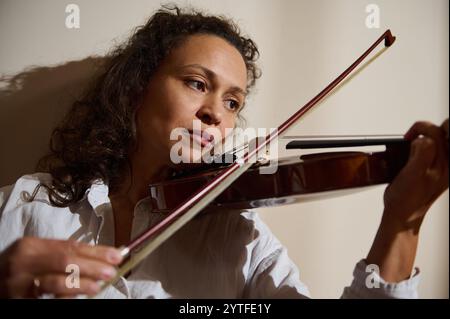 A woman intently plays the violin, showcasing passion and focus under soft natural lighting, highlighting her musical skill. Stock Photo
