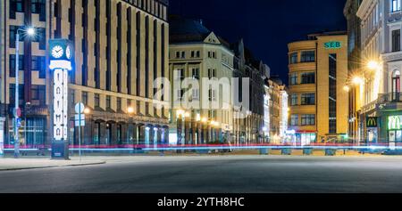 Nighttime street view in Old Riga with historic buildings, modern lights, and light trails from passing vehicles, creating a dynamic urban scene. Latv Stock Photo