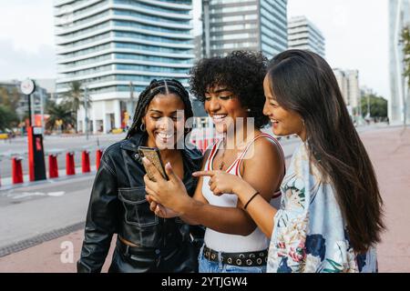 Three young women sharing a laugh while using a smartphone in the city Stock Photo