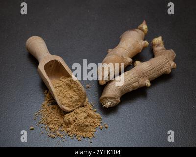 Warming ginger, root and ground with wooden spatula on dark background Stock Photo