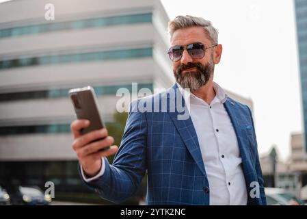 A happy mature business man using a mobile phone outside with urban city buildings in the background Stock Photo