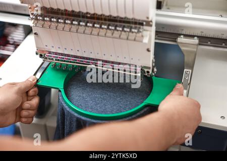 Man using embroidery machine to make design on T-shirt indoors, closeup Stock Photo