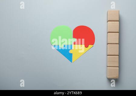 Wooden cubes and heart made of puzzle pieces on grey background, flat lay. Space for text Stock Photo