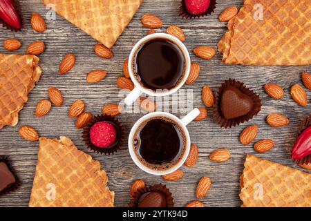 Two cups of black coffee, waffles, chocolates and almonds on a wooden table. Espresso, nuts and sweets. Top view. Stock Photo