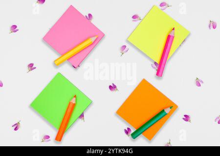 blank colorful sticky notepads with color pencils on a canvas surface covered with tiny flowers. Empty space for text Stock Photo