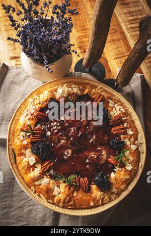 Homemade fig tart decorated with pecan nuts, almond flakes and rosemary, served in wooden bowl on festive table Stock Photo
