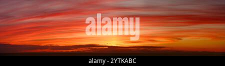 Panorama of a glowing orange sunset sky with clouds making amazing vibrant color stripes, in wide banner format Stock Photo