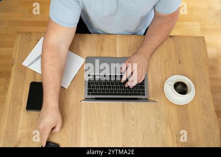 Man using a laptop on the wooden desk table top view. Stock Photo