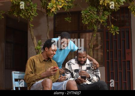 three students standing together in a school courtyard. They are engaged with their smart phones, absorbed in their devices. Stock Photo