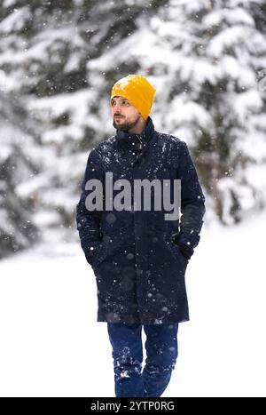 A handsome middle age man in an elegant winter fashion walking in the snowy park or forest. Stock Photo
