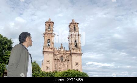 A visitor stands in front of the stunning church towers of Taxco de Alarcon, Guerrero, admiring the intricate pink stone architecture. The cloudy sky Stock Photo