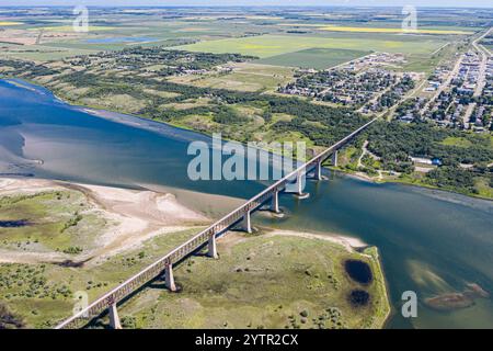 A bridge spans a river, with a town on the other side. The bridge is surrounded by a grassy area and a sandy shoreline Stock Photo