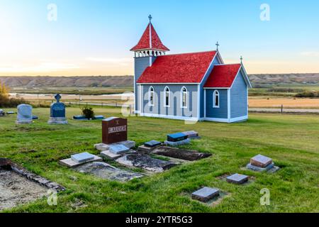 A small church with a red roof sits on a hill next to a cemetery. The cemetery is full of gravestones, and the church is surrounded by a peaceful, ser Stock Photo