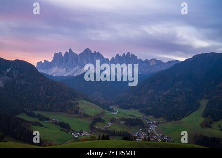 Pastel sunset over Val di Funes village with rolling green meadows and alpine farms beneath the dramatic Odle peaks, Dolomites, South Tyrol, Italy. Stock Photo