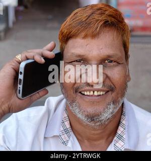A smiling, middle-aged Muslim man with henna-dyed hair in Dharavi slum area in Mumbai, India, talking on his mobile phone. Stock Photo