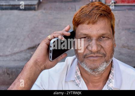 A middle-aged Muslim man with henna-dyed hair in Dharavi slum area in Mumbai, India, talking on his mobile phone. Stock Photo