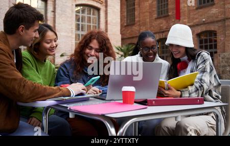 Group of multiracial student friends gathering together to study at university using a laptop. Stock Photo