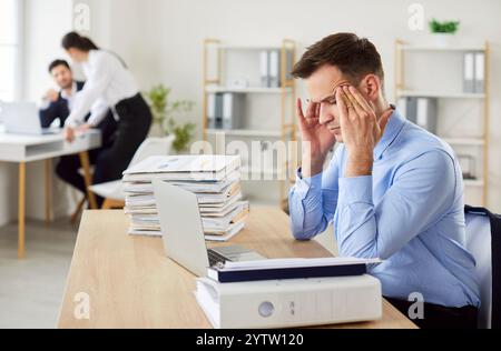 Tired young exhausted overworked business man sitting at the desk on his workplace in office. Stock Photo