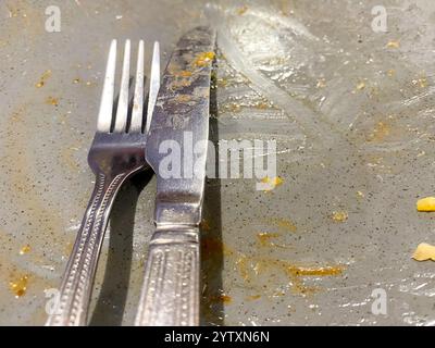 A knife and fork on a greasy plate at the end of a meal. Stock Photo