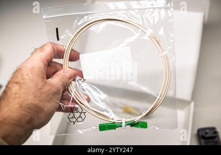 Hand holding a fiber optic cable sealed in a transparent plastic bag with green connectors, showcasing packaging and product design Stock Photo