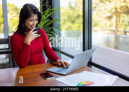 Businesswoman working using laptop online meeting in home office, Business women wearing red sweater working about new startup on laptop to analysis f Stock Photo