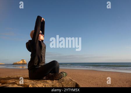woman sitting enjoying the winter sun, stretching, beach Stock Photo