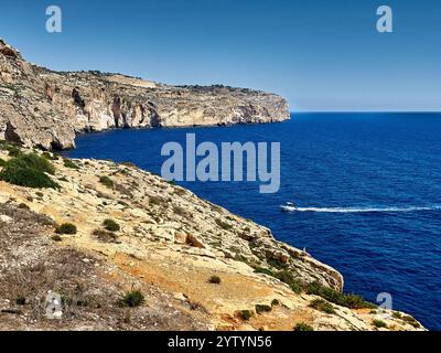 A view of the rocky coastline and the Mediterranean sea on which a boat sails, Malta Stock Photo
