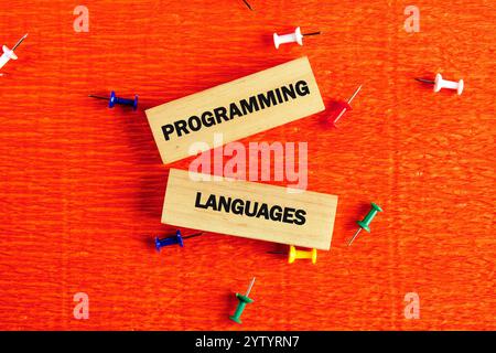 Bright orange background with two wooden blocks prominently displaying the words programming and languages. Colorful push pins scattered around create Stock Photo