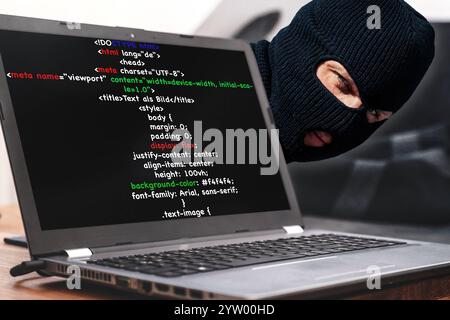 Bavaria, Germany - December 8, 2024: Hacker attack on a laptop: Illustration of cybercrime with a masked attacker and HTML code on the screen. Symbolic image of cyberattacks, data theft and the dangers of the digital world. Focus on IT security, data protection and prevention against cyber threats and cyber attacks. PHOTOMONTAGE *** Hackerangriff auf einen Laptop: Darstellung von Cyberkriminalität mit einem maskierten Angreifer und HTML-Code auf dem Bildschirm. Symbolbild für Cyberattacken, Datenklau und die Gefahren der digitalen Welt. Fokus auf IT-Sicherheit, Datenschutz und Prävention gegen Stock Photo