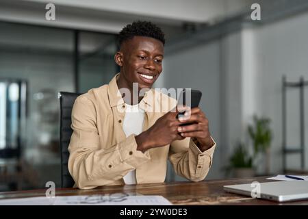 Smiling busy African business man sitting in office holding smartphone. Stock Photo