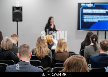 Speaker holds presentation in front of diverse audience in modern conference setting. Attendees are engaged, listening to the presentation with interest. Stock Photo