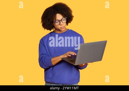 Young black man focused on work with laptop against solid yellow background Stock Photo